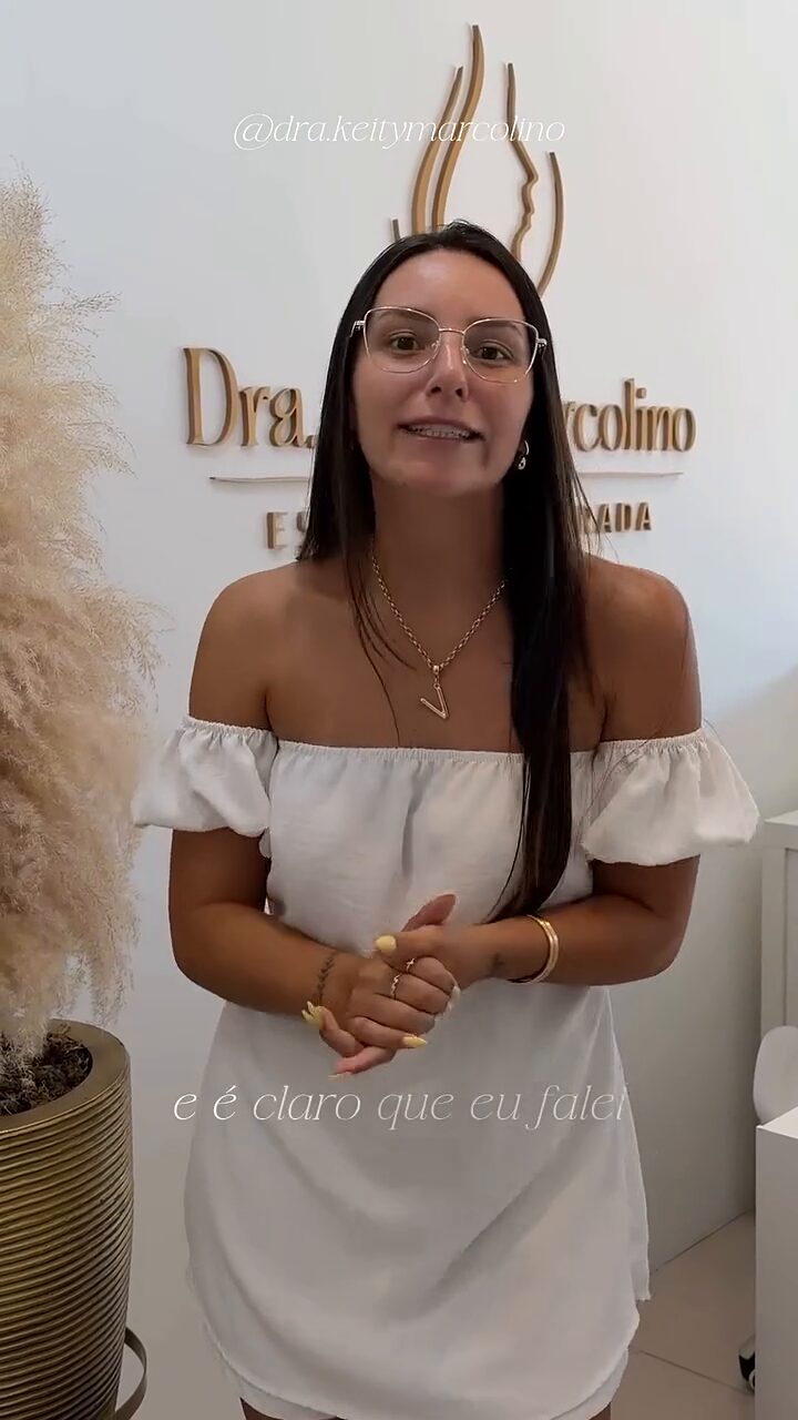 Vitória em pé na recepção de uma clínica de estética, em frente ao letreiro do consultório.