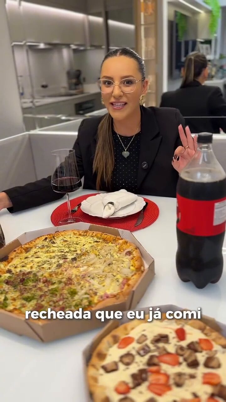 Vitória sentada à mesa de uma pizzaria, com duas pizzas servidas à frente.
